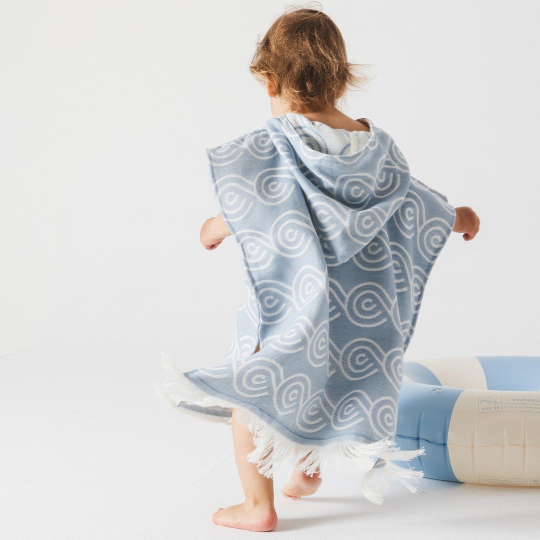 3. Child wearing light blue Patulove bamboo bath poncho with hood, shown from back, near inflatable pool ring