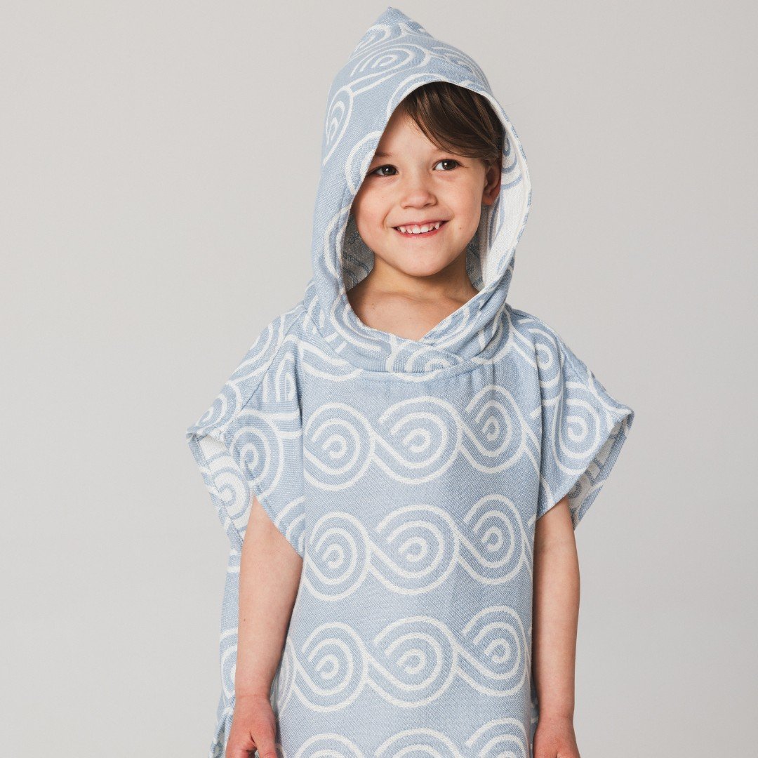 4. Child smiling in light blue Patulove bamboo bath poncho with hood and white swirl pattern, studio background