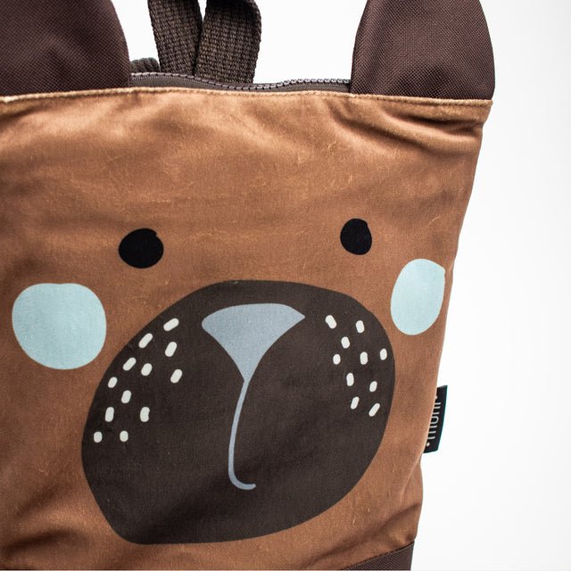 8. Child holding Muni bear backpack near a lake, wearing sunglasses, stylish outdoor look