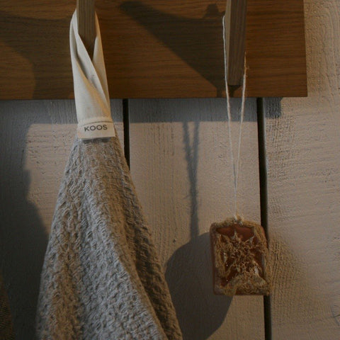 3. Grey textured linen towel hanging on wooden hook with KOOSdisain label in rustic setting