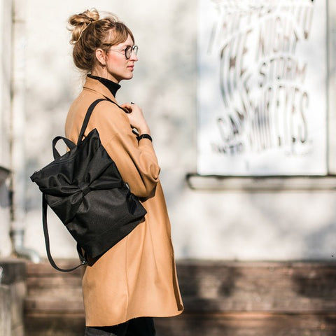 1. Woman wearing Muni Black Bow waterproof backpack in lifestyle setting, showcasing style and functionality