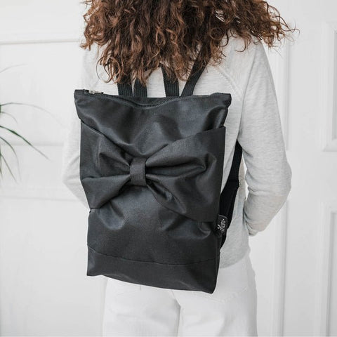 4. Woman wearing Muni Black Bow backpack indoors, showing adjustable straps and large bow detail