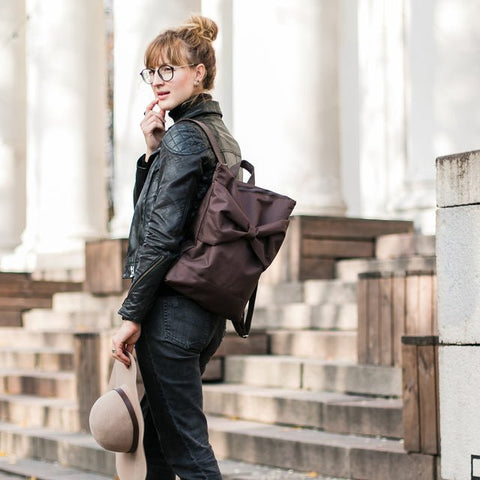 1. Woman wearing MUNI waterproof brown backpack with large bow, styled with casual outfit in urban setting