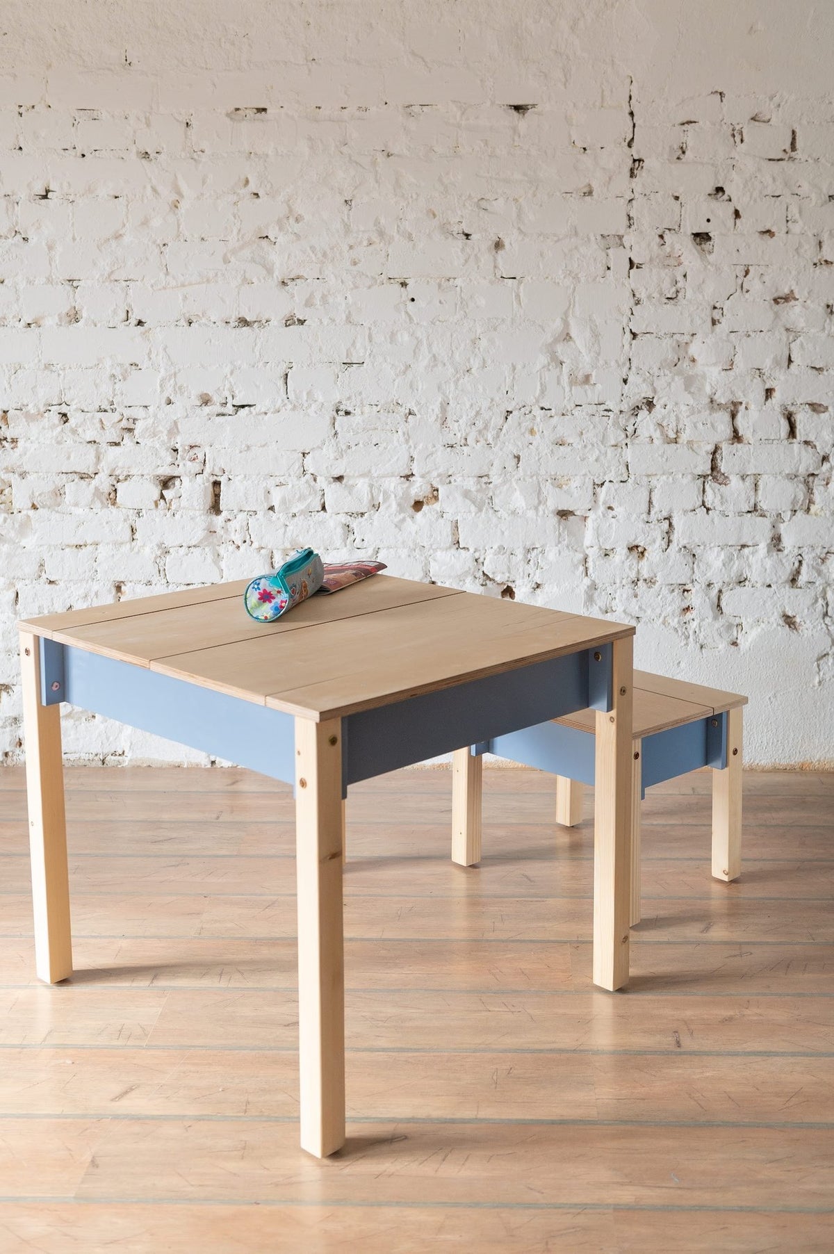 5. Blue and natural wood children's table and chair set with closed storage in a room with white brick wall