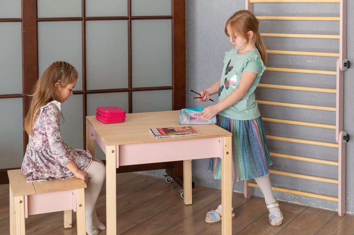 13. Two girls playing with pink and natural wood table and chair set in a room with wooden floor and gym ladder