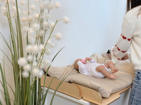 3. Baby lying on beige changing table mat with woman adjusting in nursery