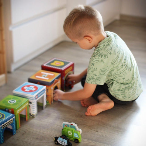 3. Boy arranging colorful city-themed puzzle cubes with wooden vehicles on a wooden floor