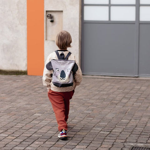 1. Child wearing Muni Koala backpack walking on cobblestone street, showcasing playful design and adjustable straps