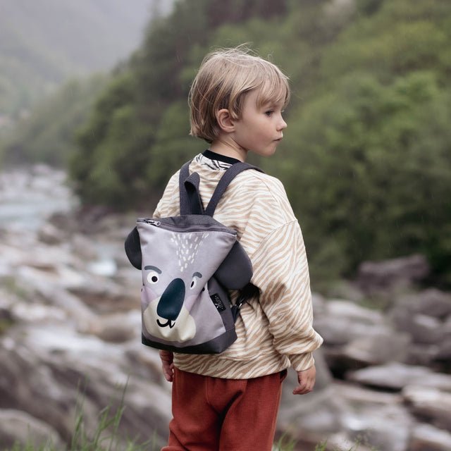 4. Child with Muni Koala backpack by river, showcasing outdoor adventure and adjustable straps