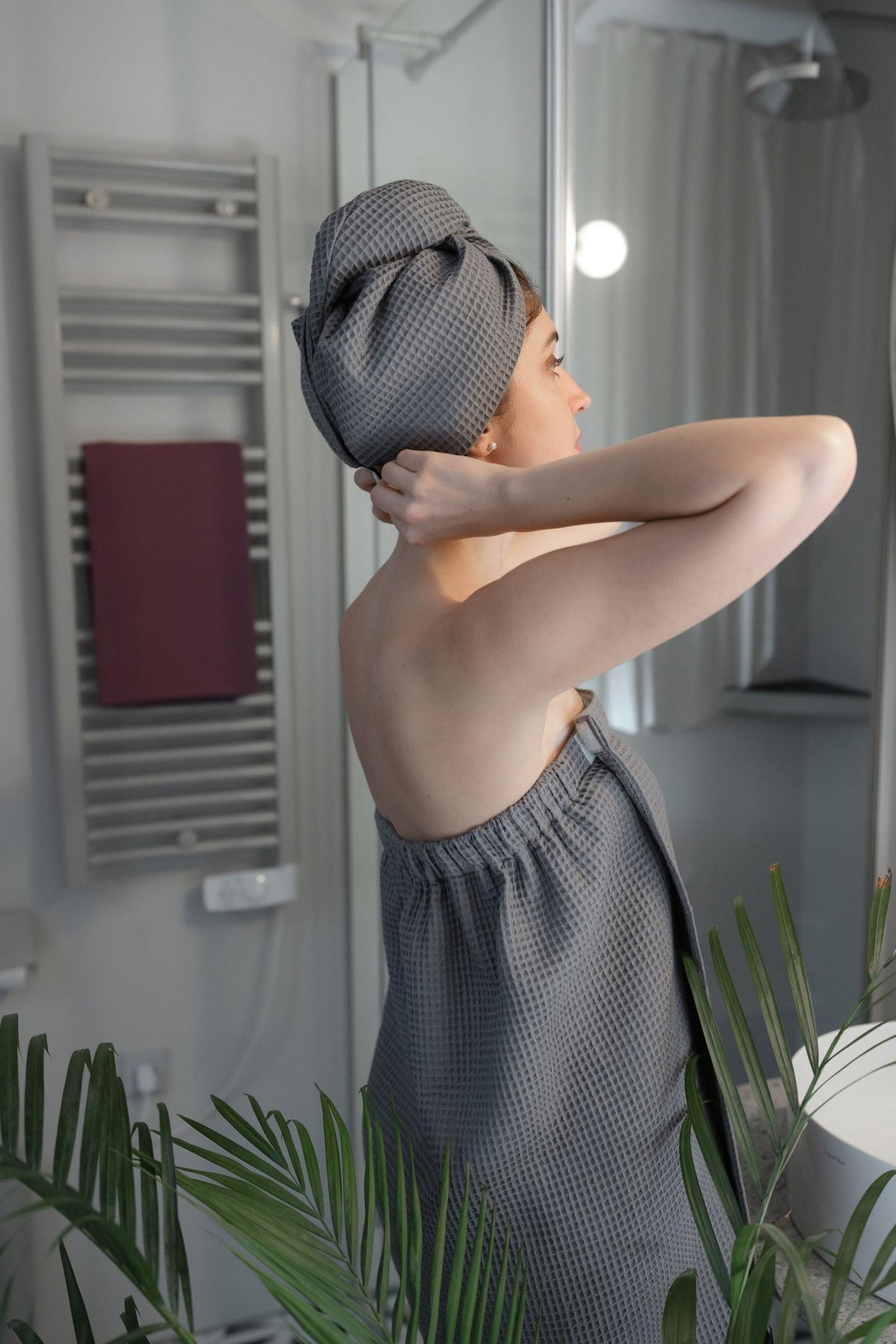 1. Woman in gray cotton waffle sauna wrap with matching head wrap, adjusting hair in bathroom setting