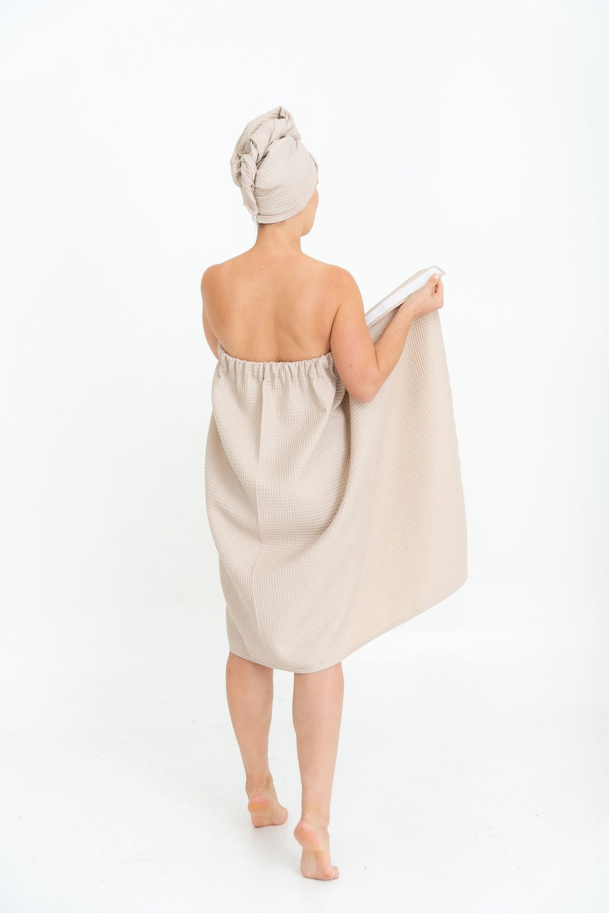 1. Woman in beige cotton waffle sauna wrap with matching head wrap, shown from back in studio setting