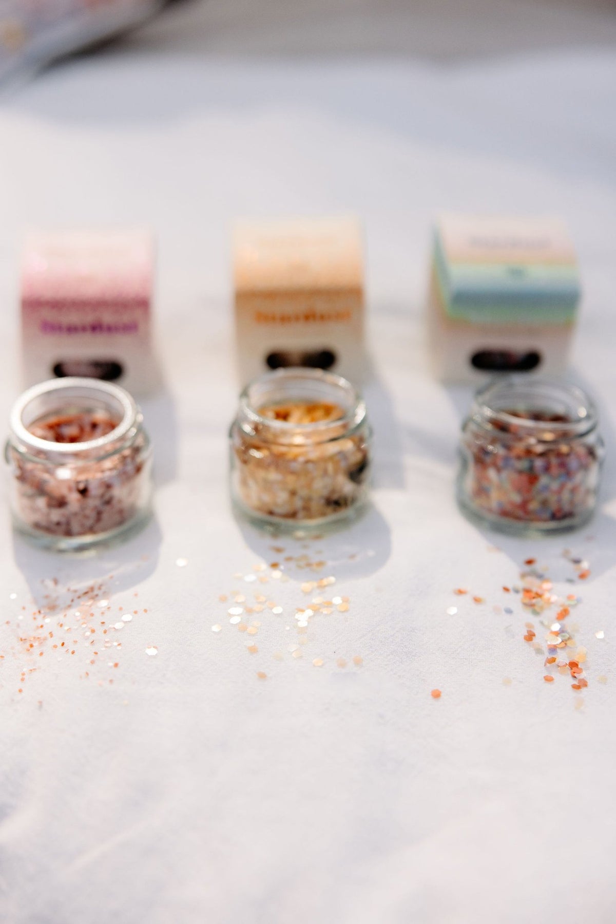 4. Three glass jars of decorative eco glitter in different colors, with packaging, displayed on a light surface