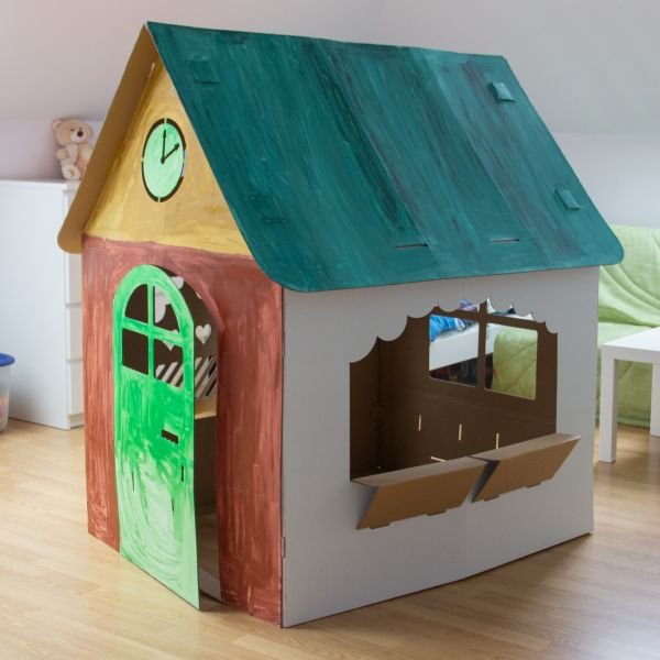 9. Colorfully painted SEIK cardboard house for kids with green door and clock, shown indoors