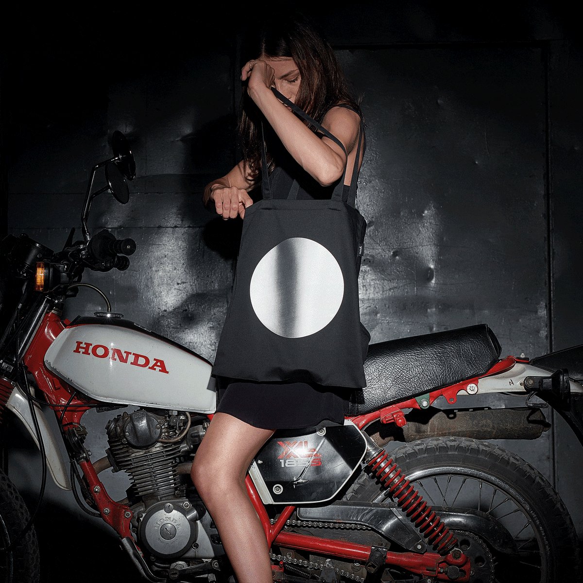 1. Women's MARCH Reflective Tote DOT in lifestyle setting, shown with motorcycle, highlighting reflective print
