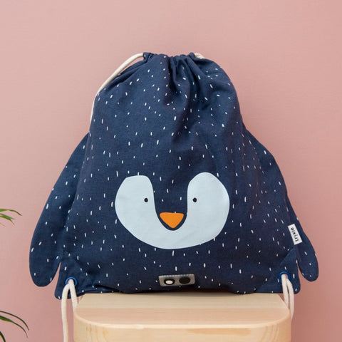 1. Trixie Baby's Mr. Penguin drawstring bag in navy with penguin face design, displayed on a wooden stool against a pink background