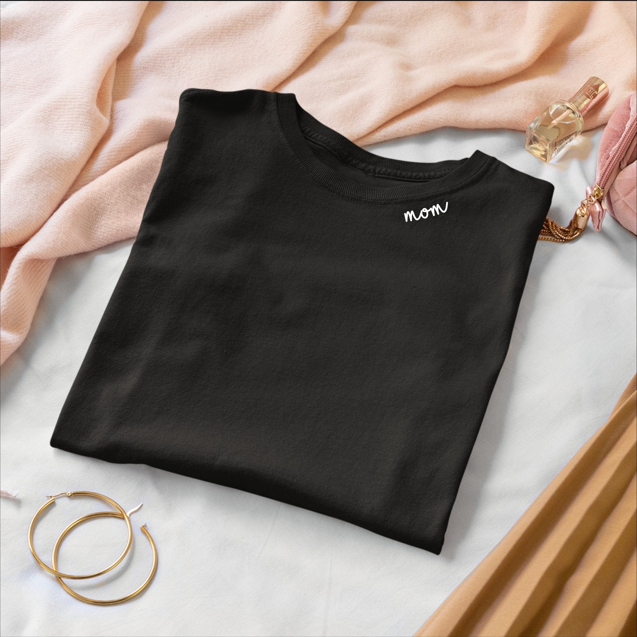 1. Black organic cotton t-shirt with 'mom' embroidery, folded with accessories in lifestyle setting