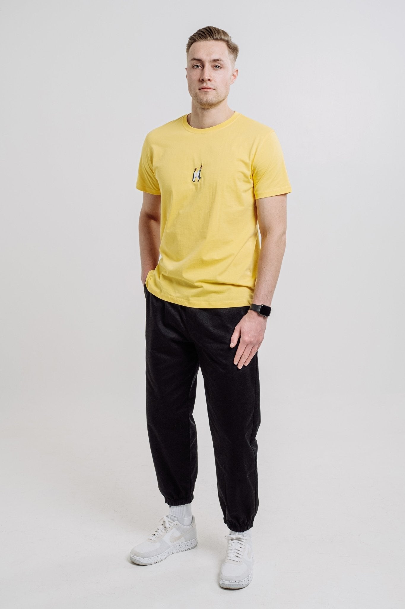 1. Unisex yellow Emperor Penguin T-shirt by Sossu worn by male model in studio, showcasing relaxed fit