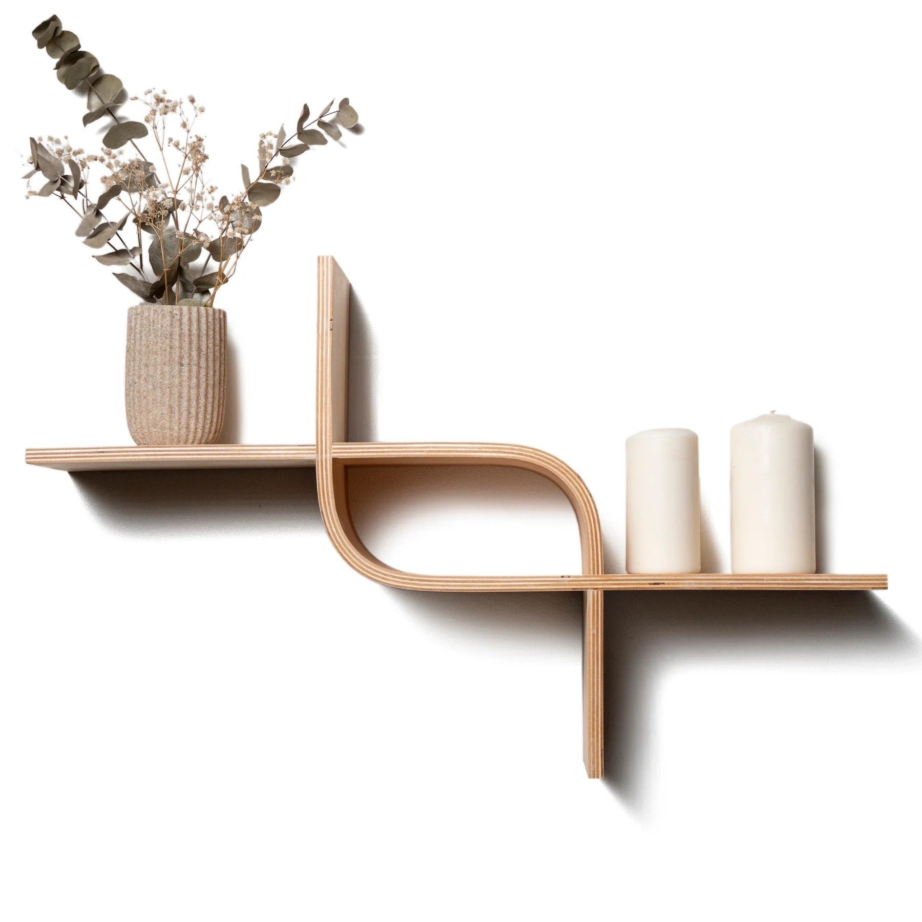 1. Wooden floating shelf with wave-inspired design holding a vase with dried flowers and two white candles against a white background