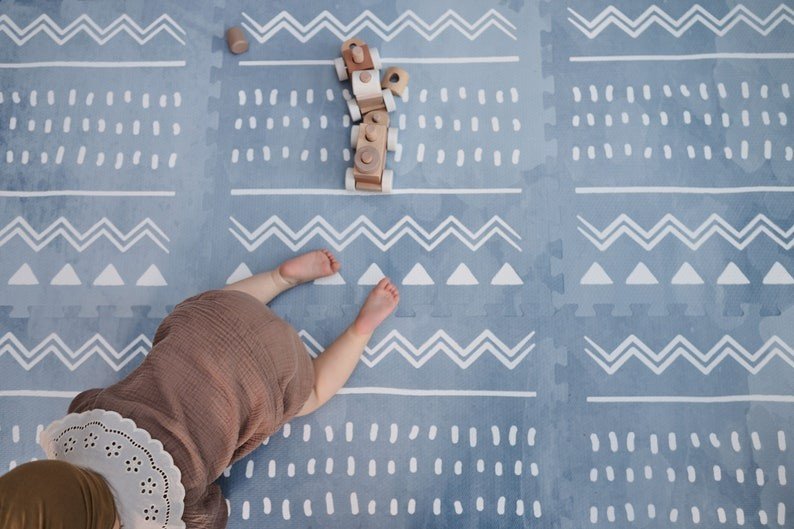 1. Baby crawling on blue OLYA KIDS Boho puzzle playmat with geometric patterns, surrounded by wooden toys