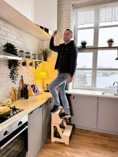 1. Man standing on wooden folding seat and climbing helper in kitchen to change lightbulb