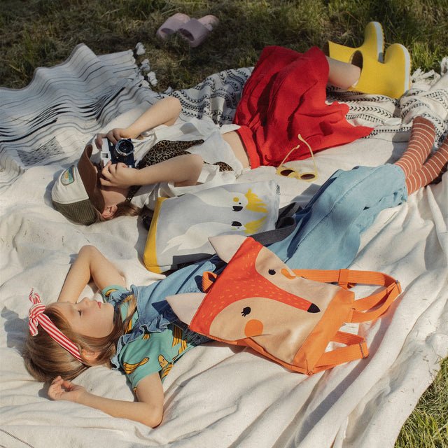 2. Muni kids fox backpack on picnic blanket with children, highlighting outdoor adventure setting