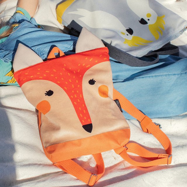 12. Muni kids fox backpack on grass, highlighting vibrant orange color and playful design