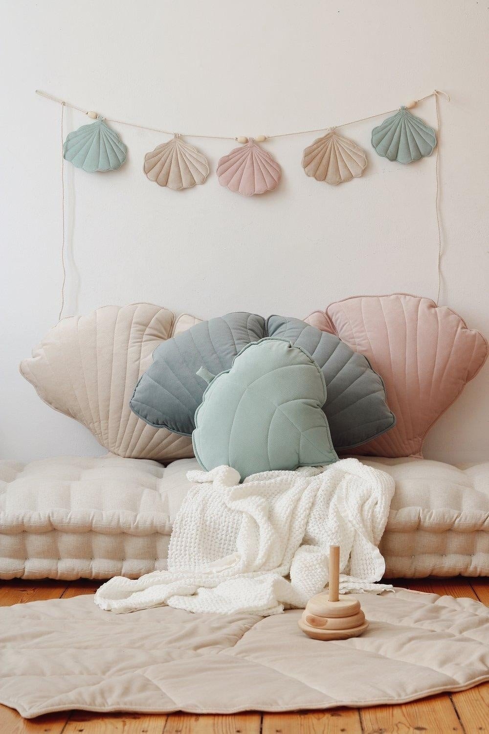 2. Pastel shell garland hanging above a seating area with shell cushions and a soft blanket in a child's room