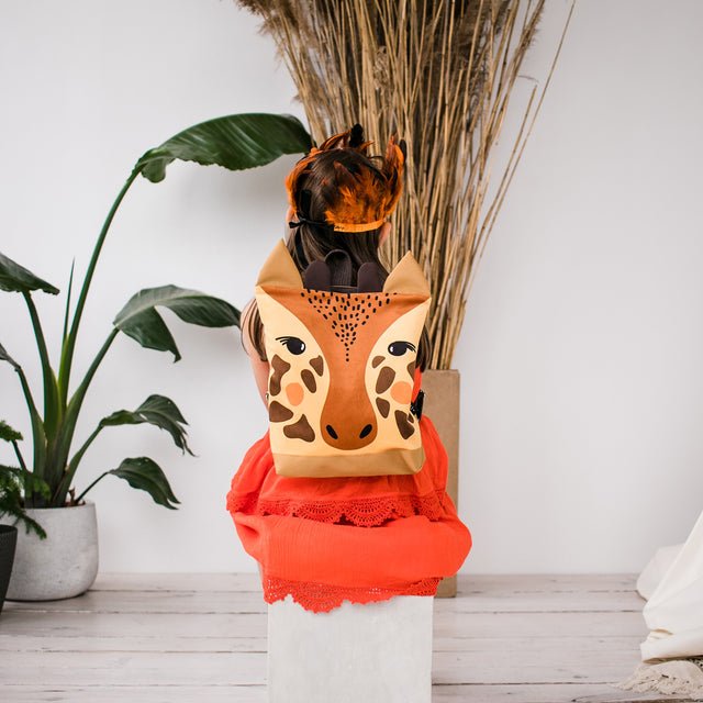 2. Child sitting with Muni giraffe backpack, highlighting velvet fabric and giraffe design