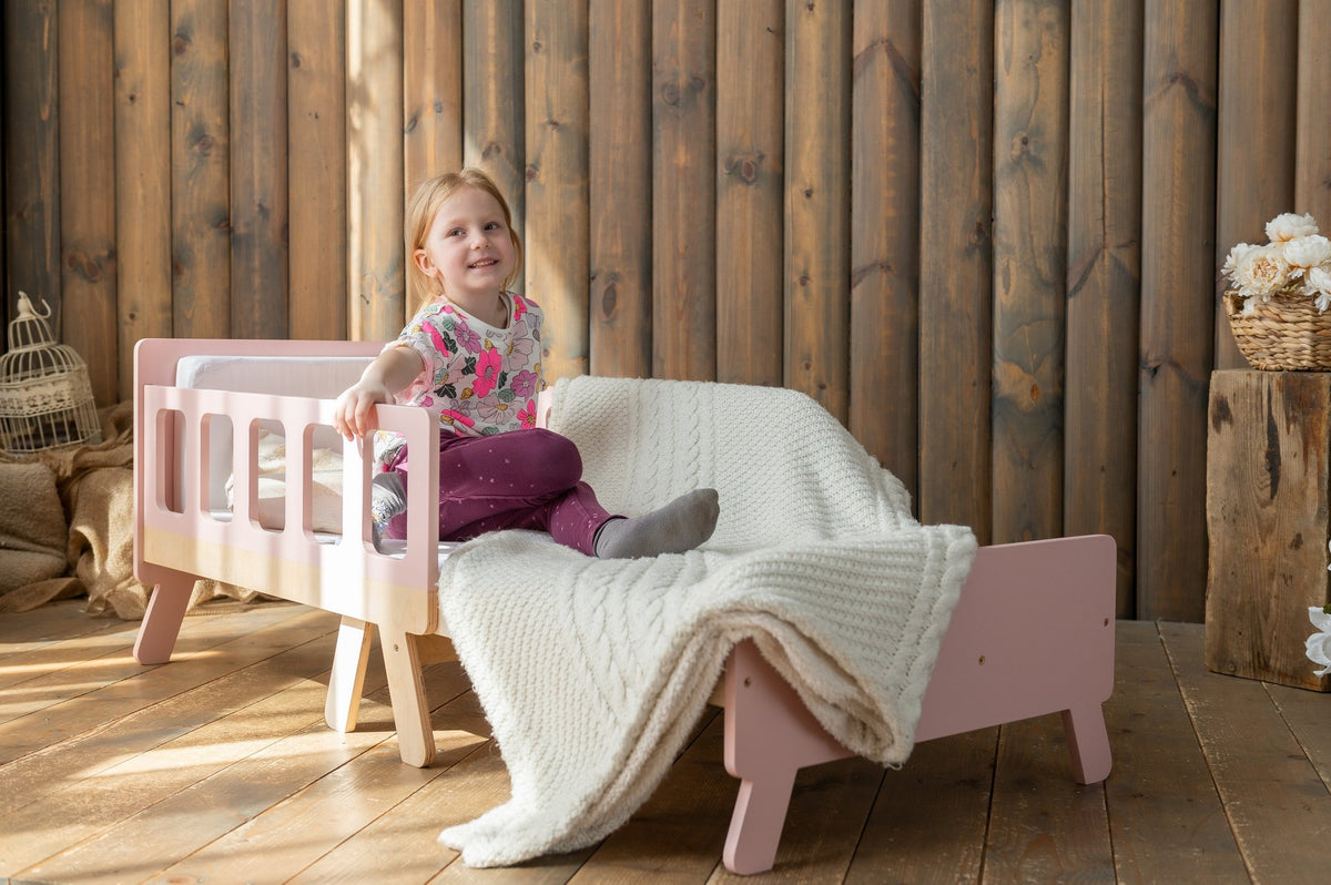 15. Child sitting on pink growing bed with white blanket in wooden room
