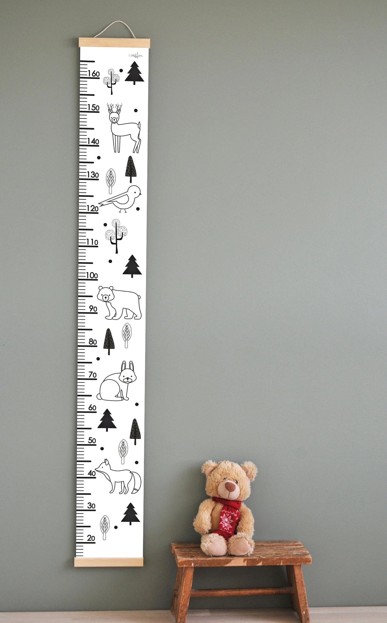 1. Black and white kids' growth chart with wild animal illustrations, including deer and bear, hanging on a wall with a teddy bear on a stool below, featuring wooden slats and attached string for easy hanging.