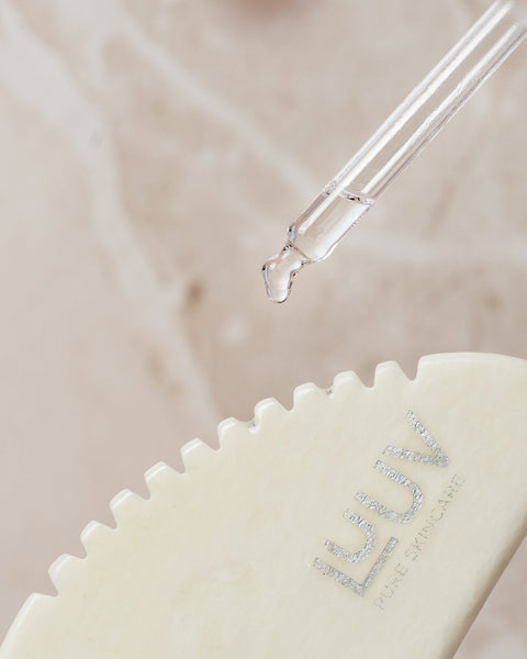 2. Close-up of LUUV Gua Sha for Body with toothed edge and dropper applying oil, highlighting jade texture and brand logo