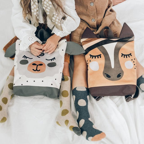 1. Kids wearing Muni sheep and animal-themed backpacks, sitting on a bed, showcasing playful designs