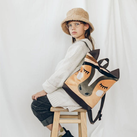 4. Girl sitting on stool with Muni horse backpack, showing side view in lifestyle setting