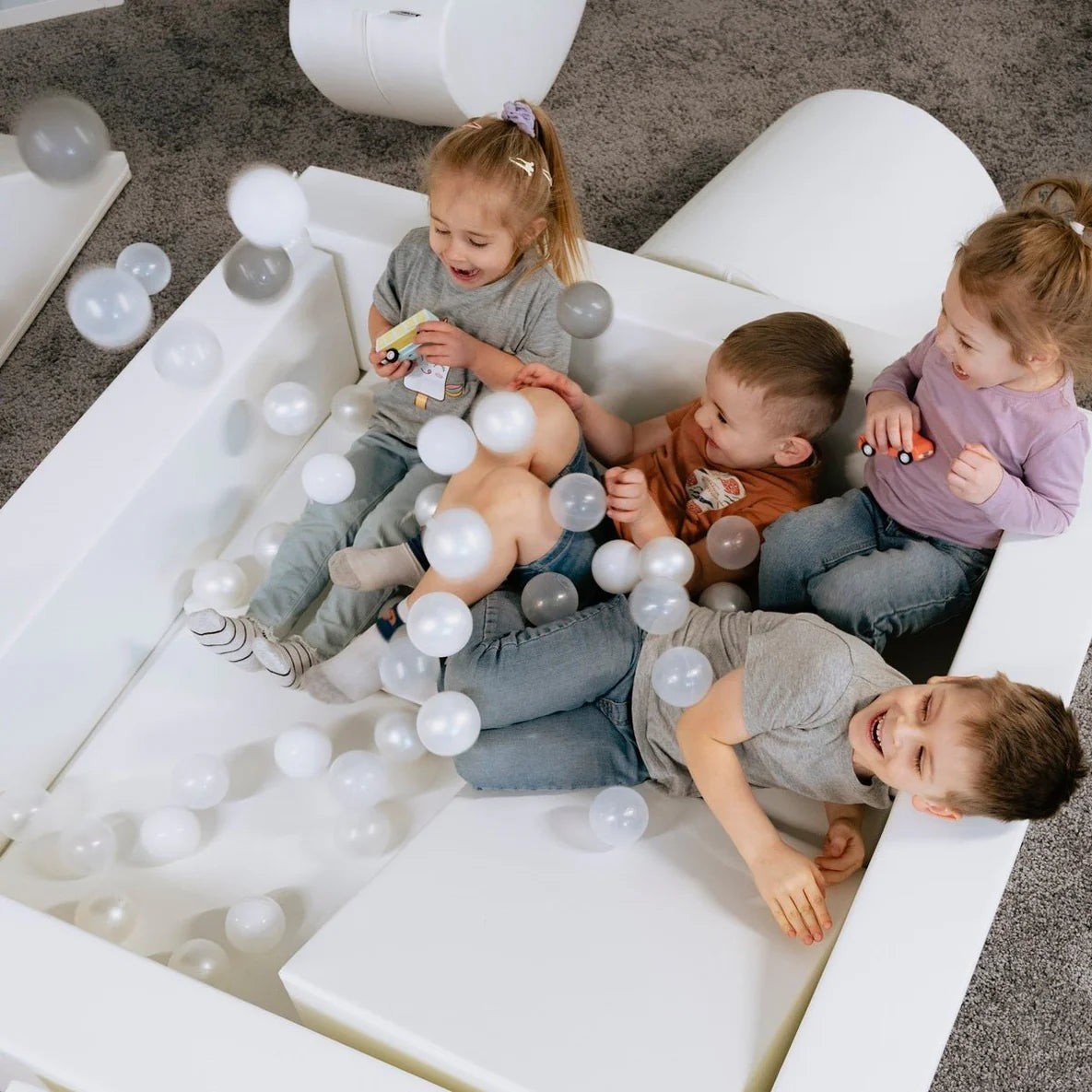 1. Three children playing in a white ball pit filled with IGLU soft play balls in pastel colors, creating a fun and sensory-rich environment