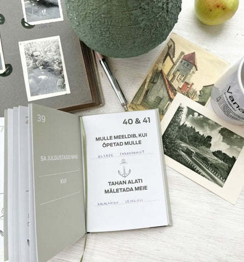 1. Lifestyle image of SEIK's '100 Asja, Mida Vanaisa Juures Armastan' book surrounded by vintage photos and a mug, ideal for capturing memories with grandfather