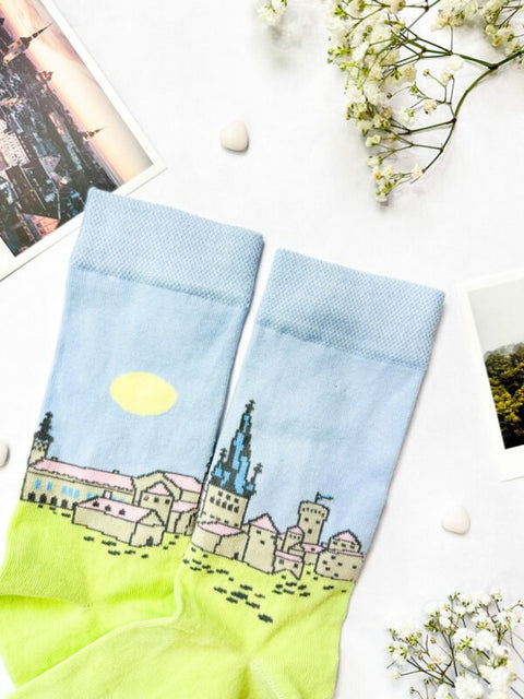 2. SEIK Old Town Tallinn socks featuring colorful cityscape design, displayed flat with postcards and flowers
