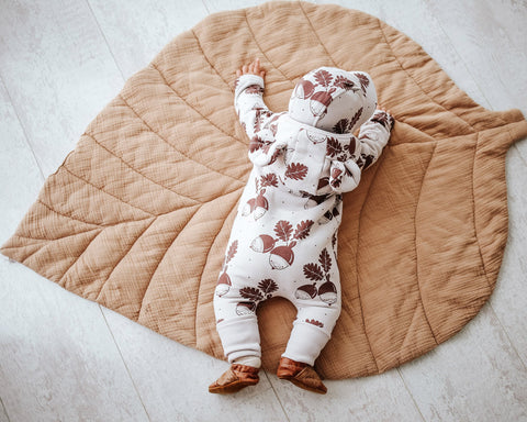 2. Baby in Zezuzulla eared jumpsuit with acorn print, lying face down on a leaf-shaped mat