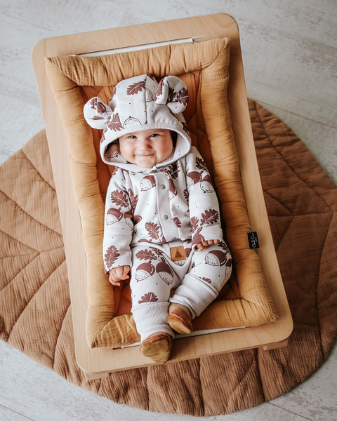 1. Baby wearing Zezuzulla eared jumpsuit with acorn print, lying on a cushioned mat