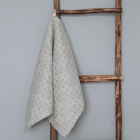 1. Beige kitchen towel with Hiiumaa folk art pattern hanging on rustic wooden ladder, made of 52% linen and 48% cotton by LOKO, designed in Estonia