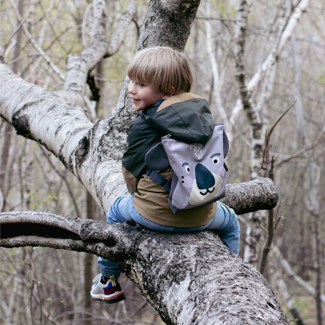 5. Child sitting on tree branch with Muni Koala backpack, highlighting playful design and outdoor use