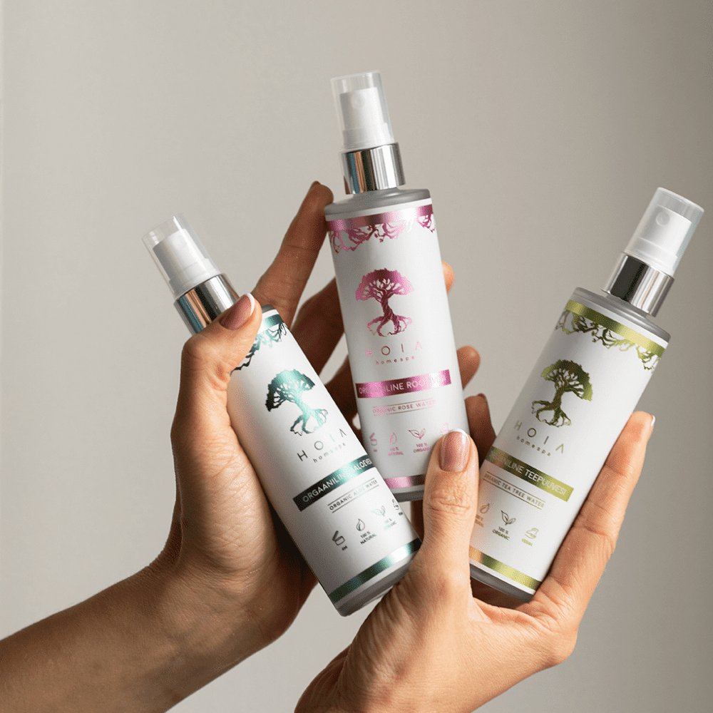 2. Hands holding HOIA homespa Organic Tea Tree Water and other variants, showcasing eco-friendly skincare collection