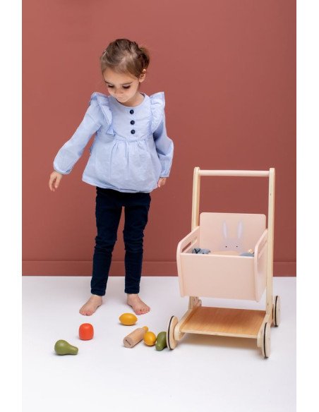 3. Child playing with Trixie Baby Wooden Shopping Cart, surrounded by toy fruits on pink background