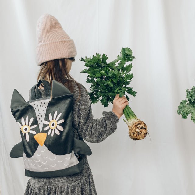2. Girl with Muni owl backpack in lifestyle setting, holding celery