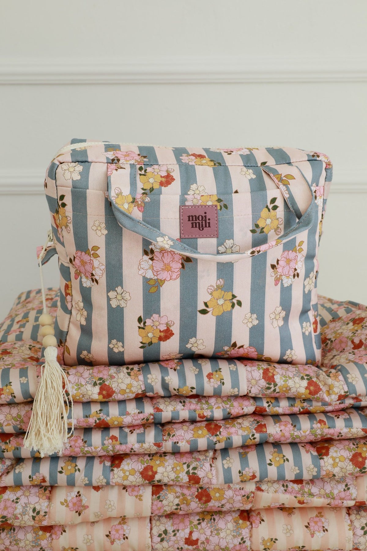 4. Large blue striped makeup bag with floral print and moi mili logo, placed on matching fabric