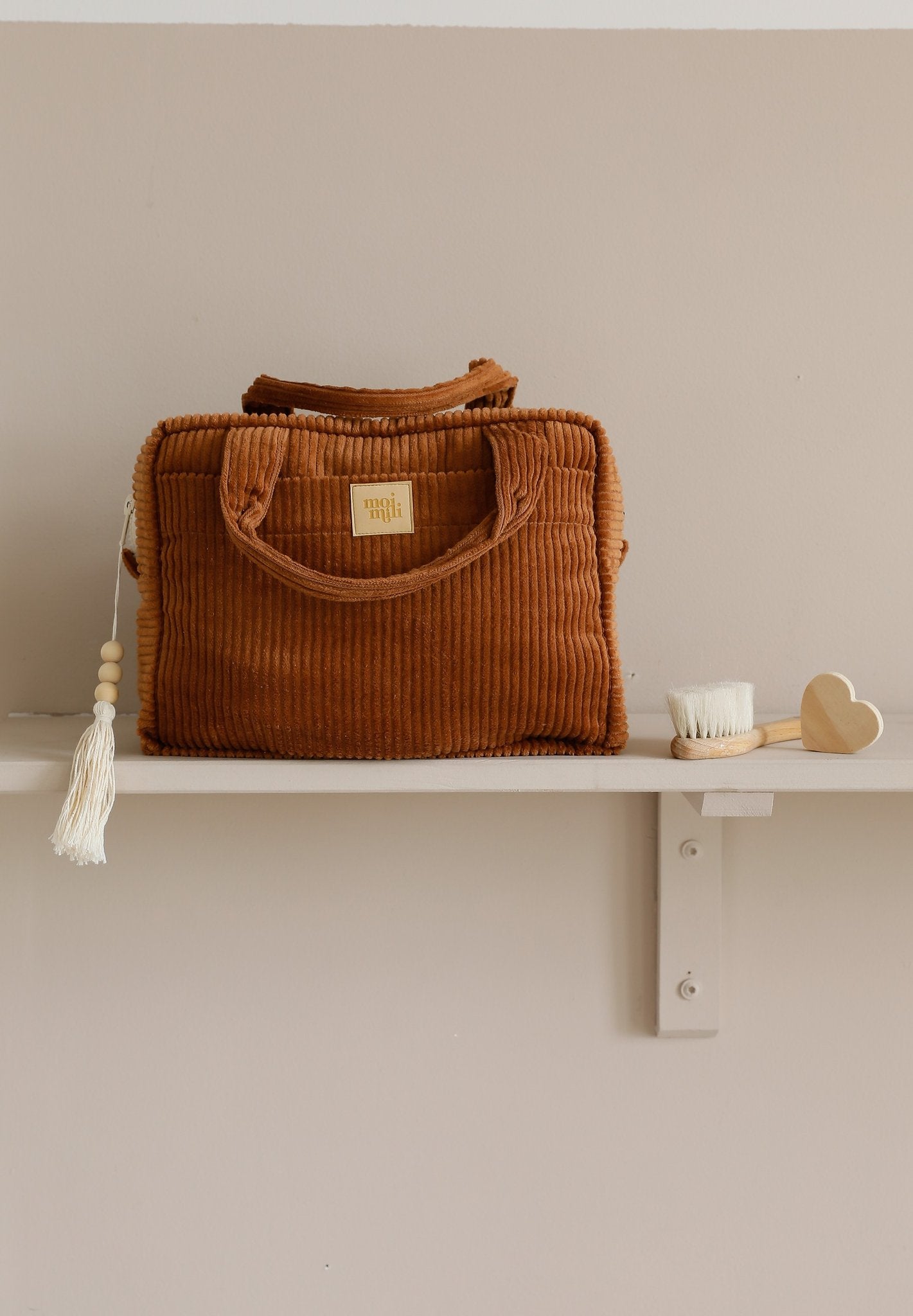 1. Caramel-colored large makeup bag with tassel detail on a shelf, next to a brush and heart-shaped item, showcasing its versatile design