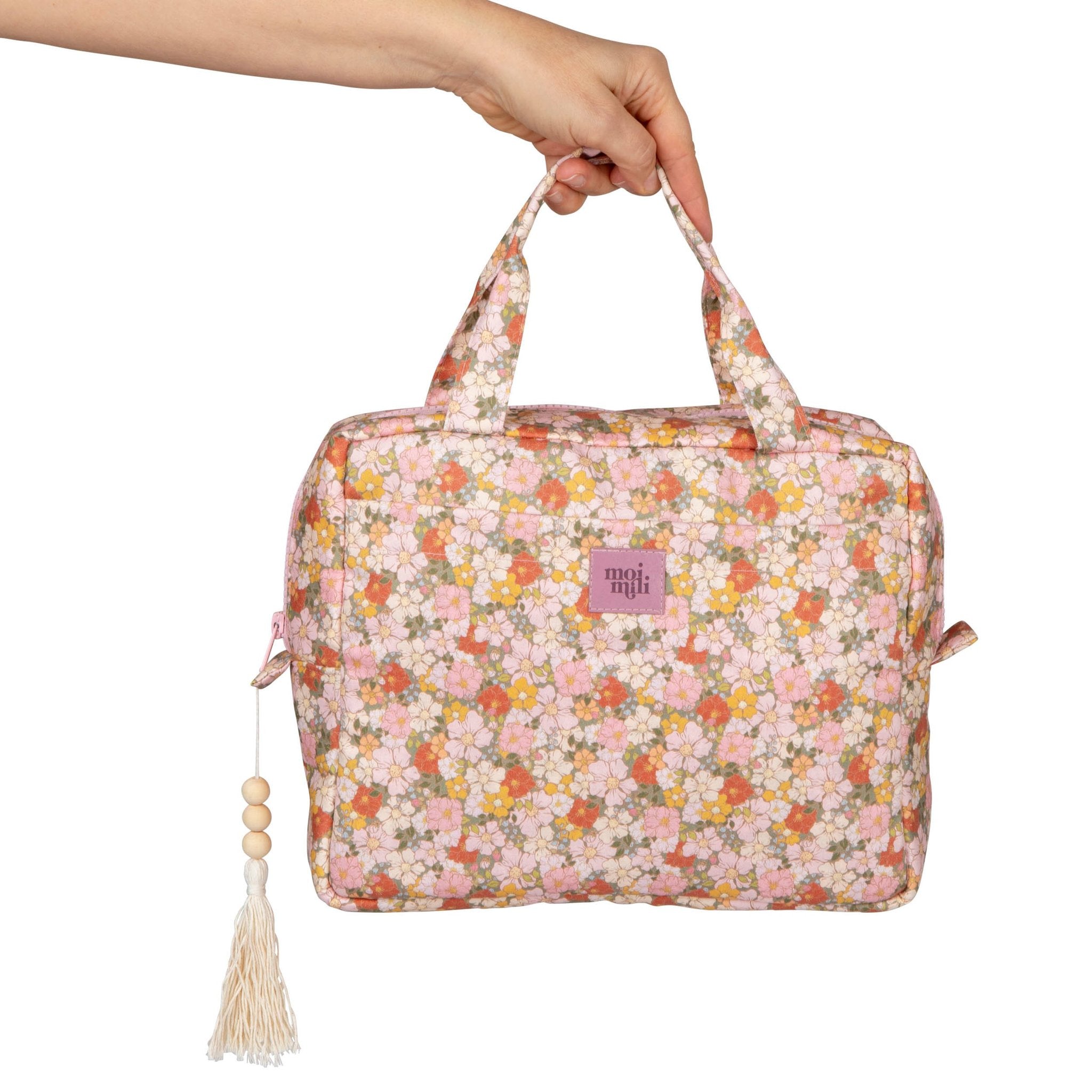 1. Hand holding Moi Mili large makeup bag with floral print and tassel detail against white background
