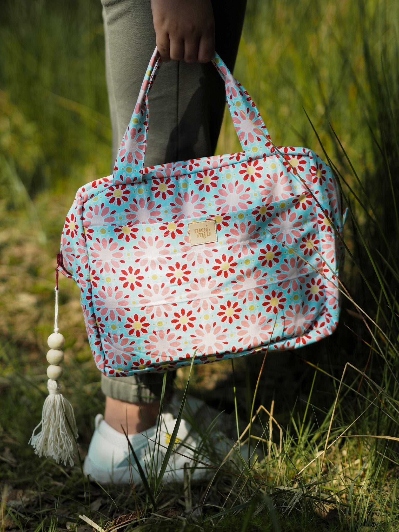 1. Person holding Moi Mili large makeup bag with red flower print in outdoor grassy setting