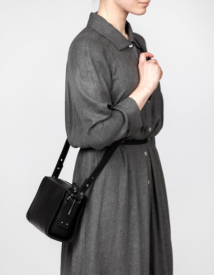 1. Woman wearing black Stella Soomlais Treasure Box handbag with adjustable strap over shoulder, dressed in grey dress, studio setting