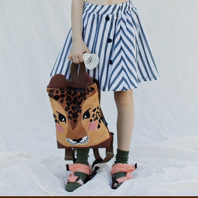 4. Child holding Muni leopard backpack, styled with striped skirt in lifestyle setting