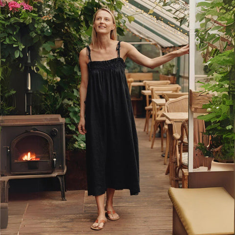 1. Woman wearing black linen Ballade dress with tie spaghetti straps in a cozy indoor garden setting